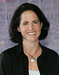 Lynn Novick smiles at the camera. She has short brown hair and is wearing a black jacket.