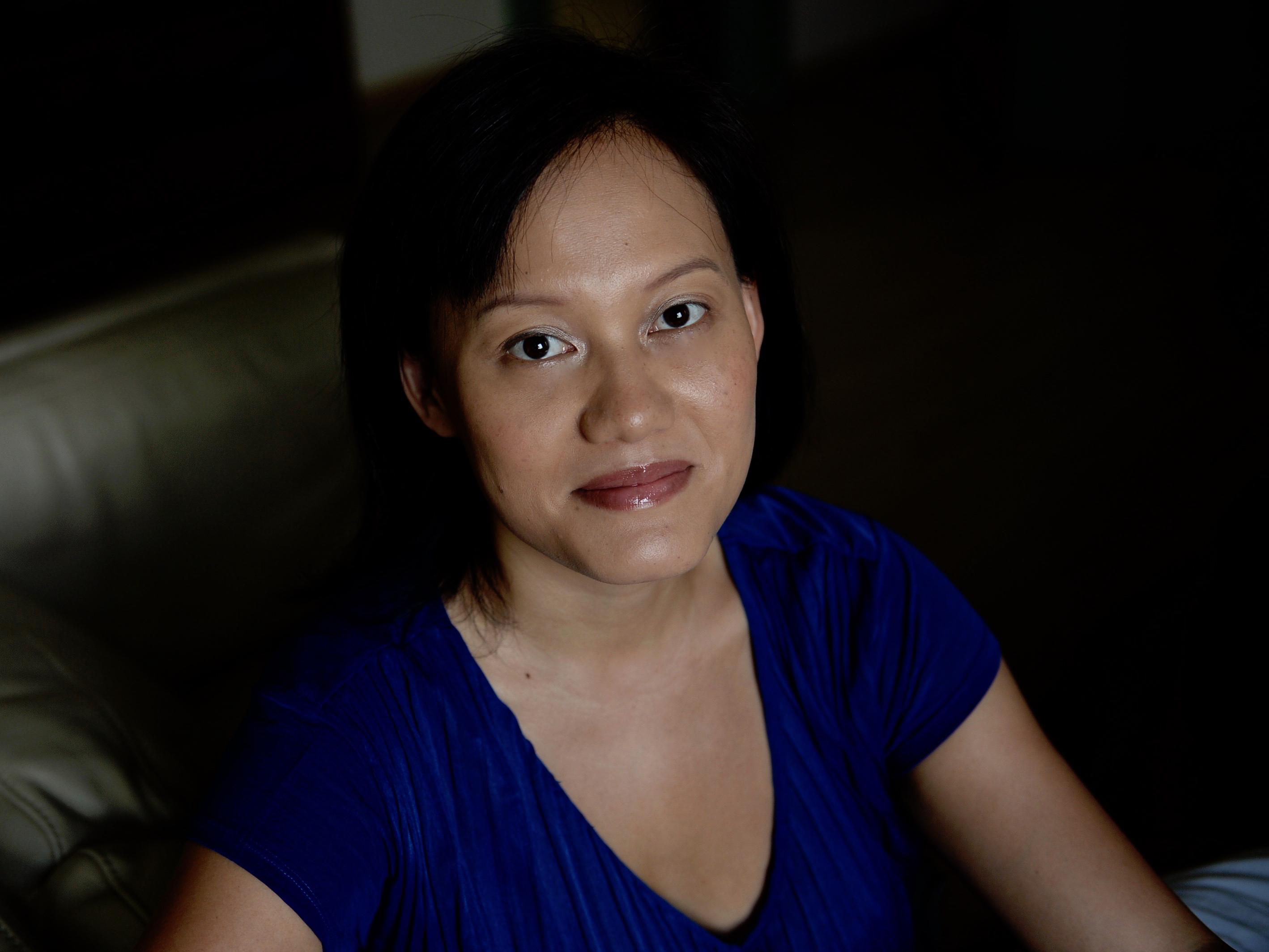 Eunice is in front of a dark background, she looks at the camera slightly with a very subtle smile. She has a dark top and medium-length hair.