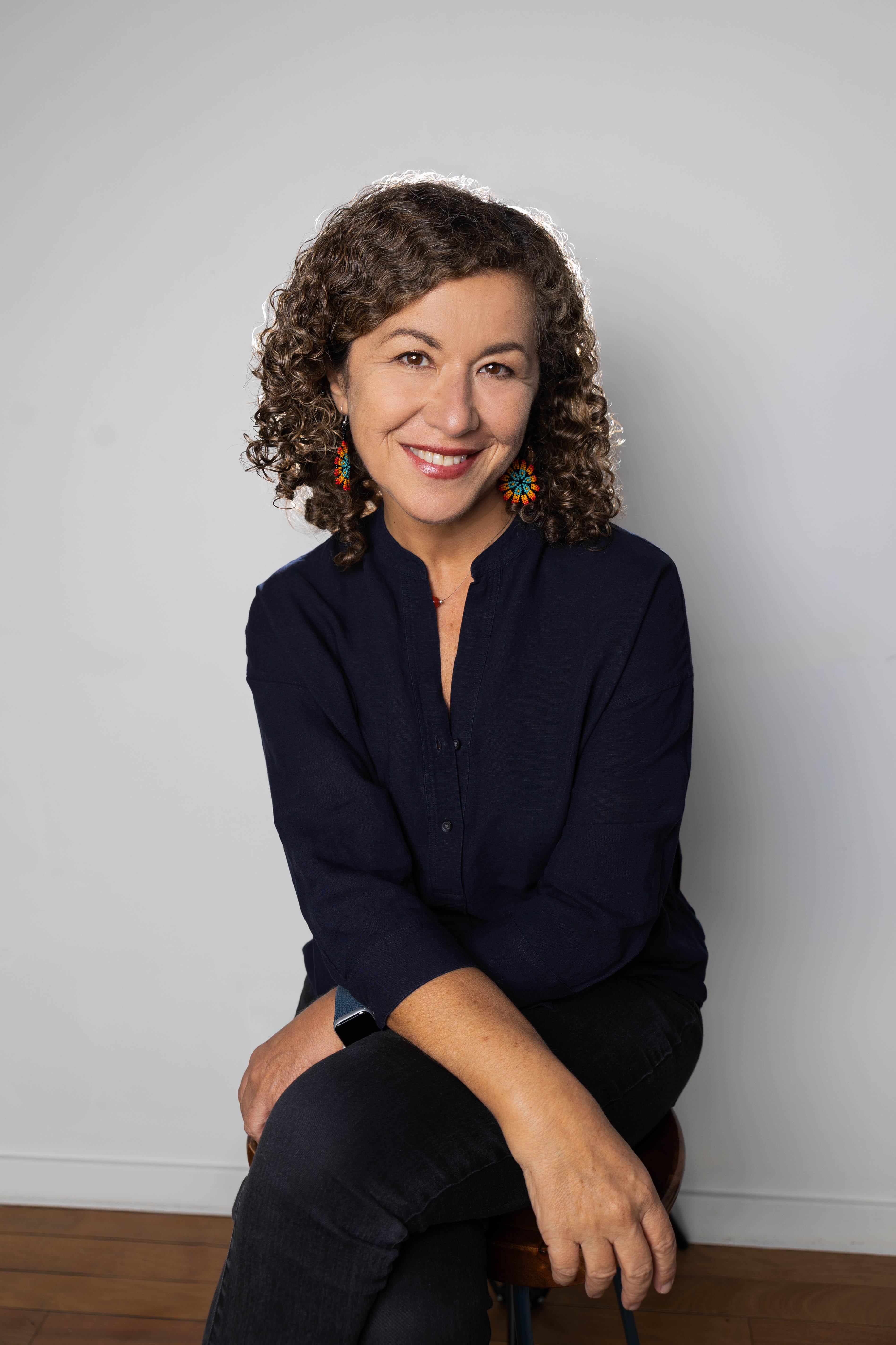 A woman wearing multicolored earrings smiles in front of a black backdrop.