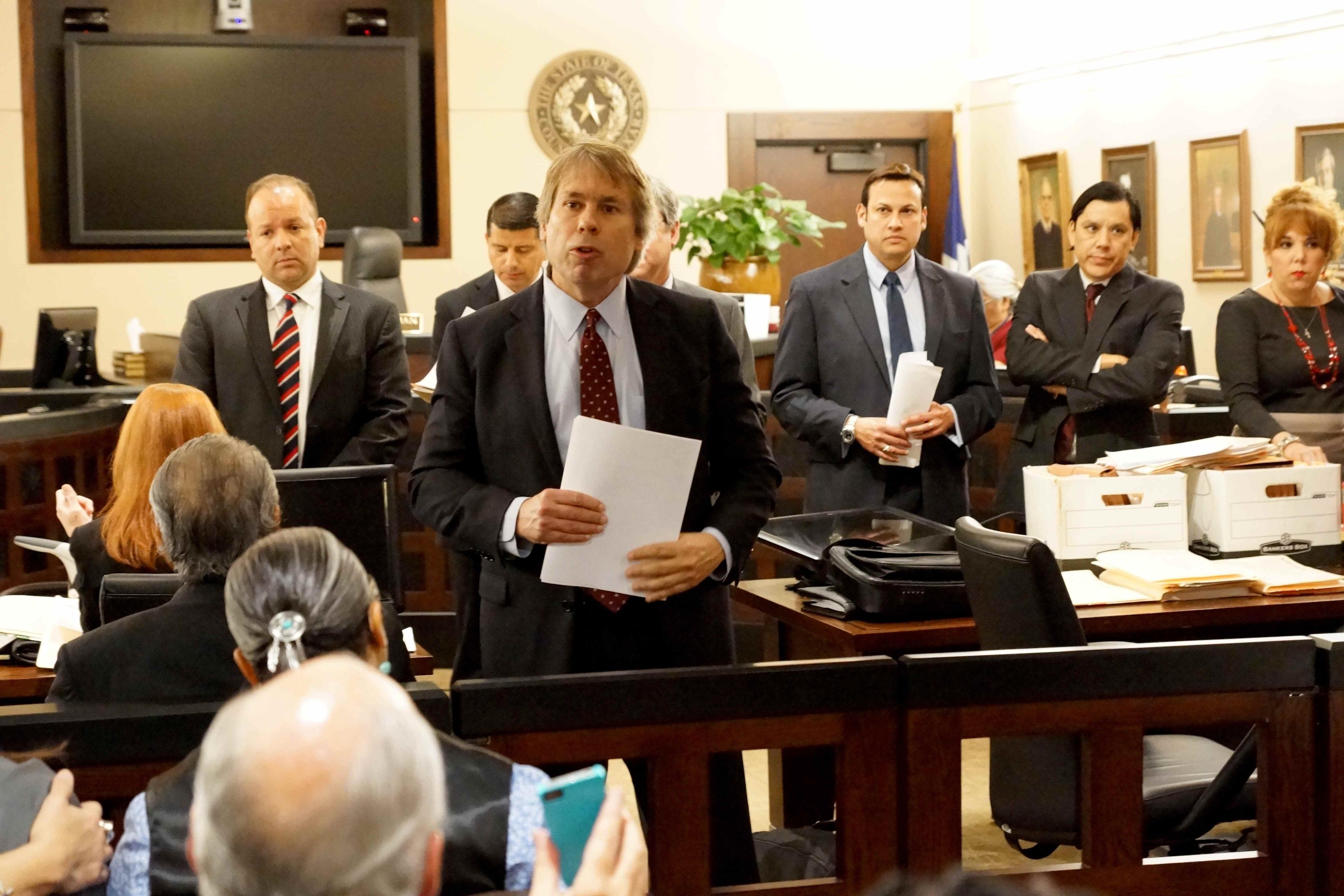 Still from Southwest of Salem. A man in a suit addresses the court, behind him there are six persons in a suit.