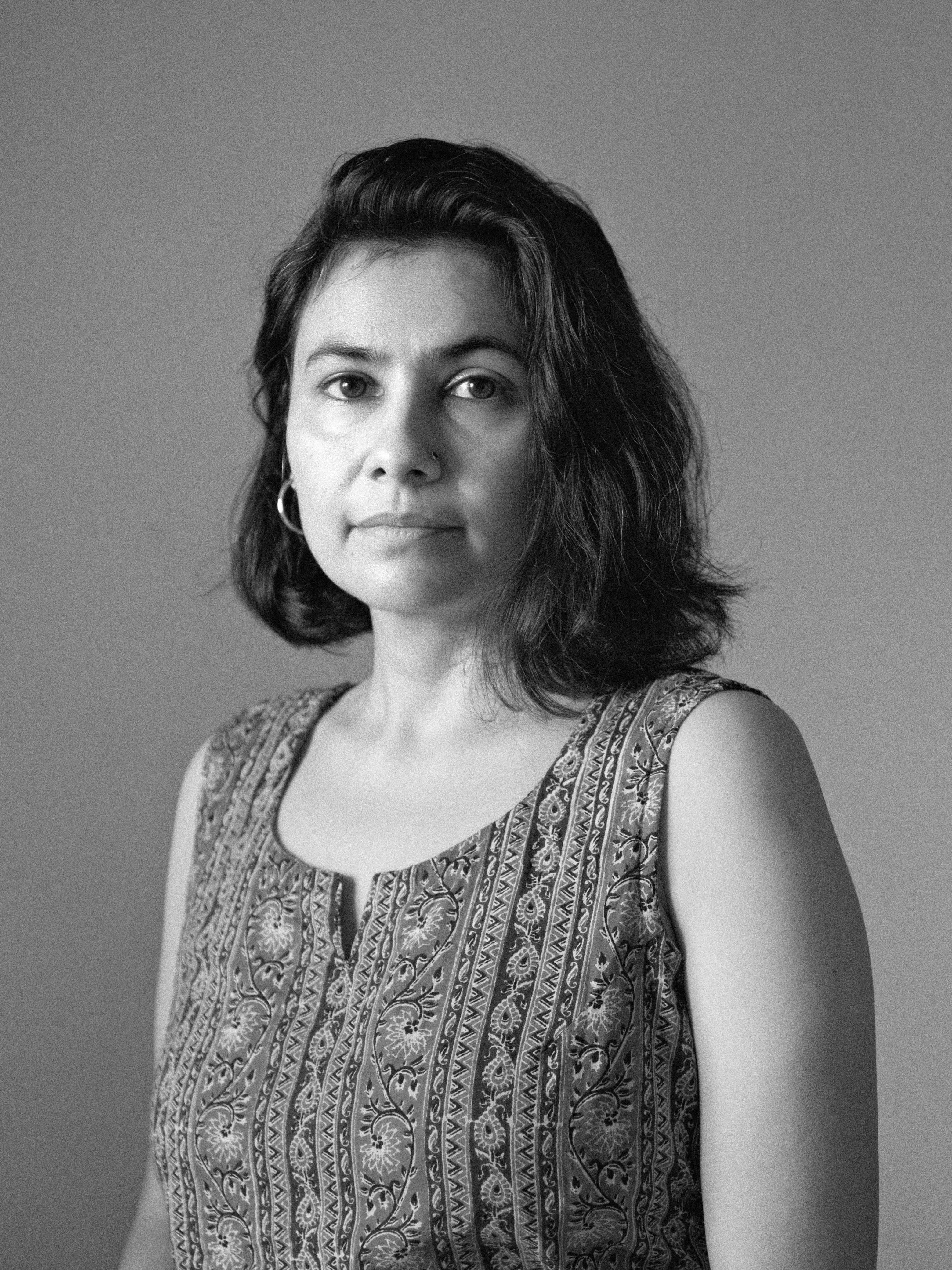 Black and white portrait of woman with mid-length hair looking at camera, wearing a decorative sleeveless shirt.