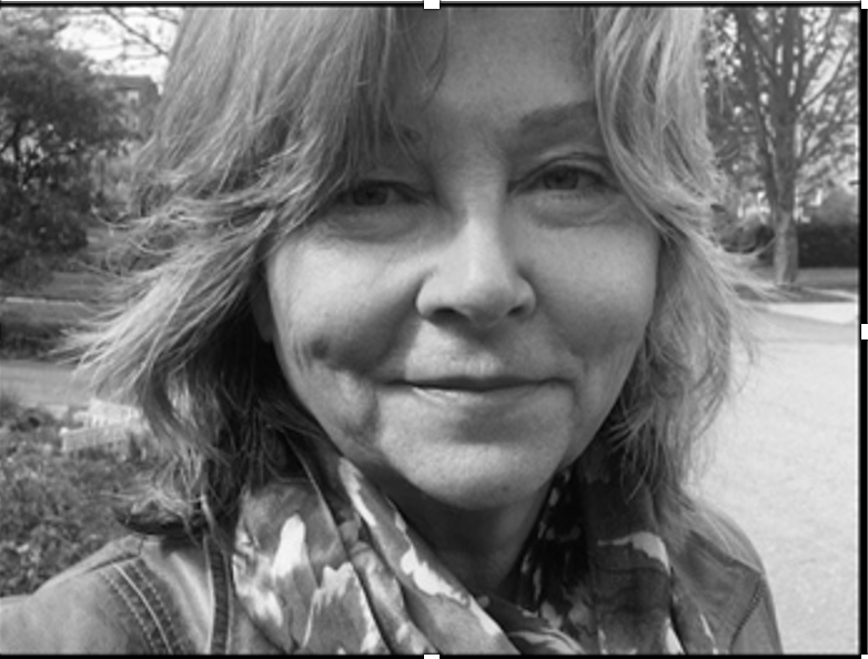 Corinna Sager looking directly at the camera. She has shoulder-length light brown hair and is wearing a scarf. Black and white portrait.