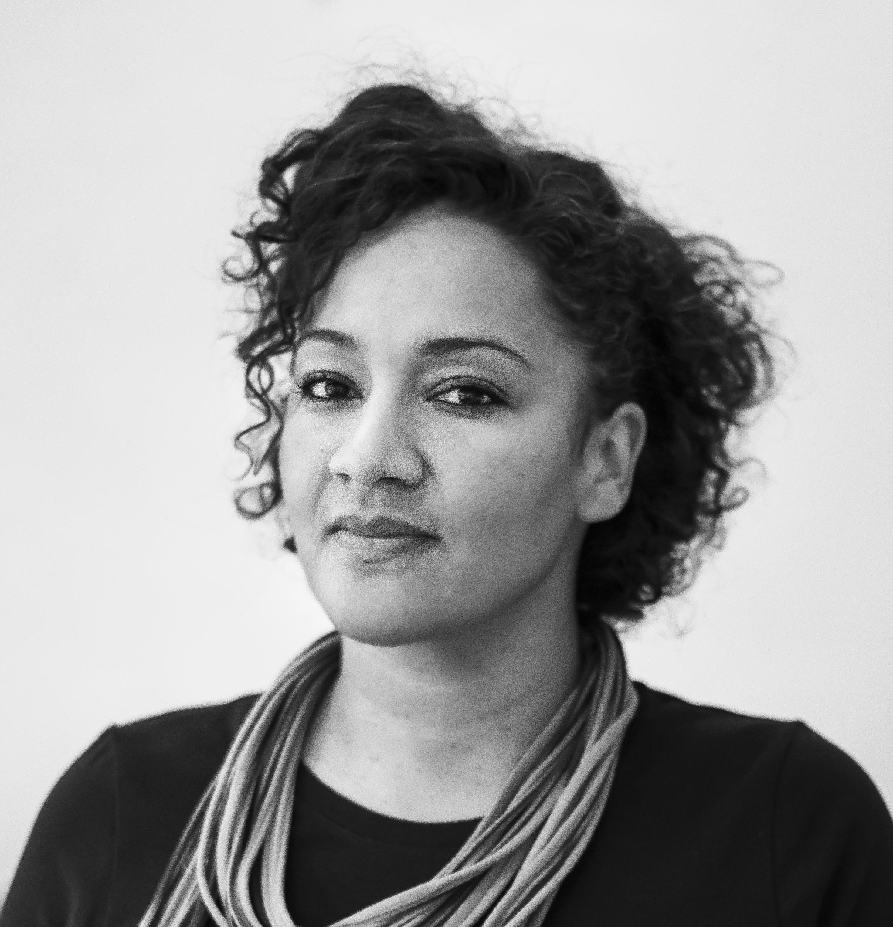 Maia Lekow headshot. Headshot of a woman with curly short hair, a long sleeve shirt and a necklace, looking at the camera