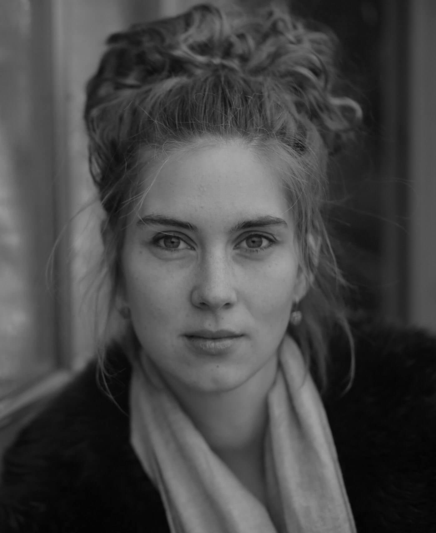 The director of Twice Colonized, Lin Alluna, looking into the camera. She's a caucasian woman with red hair, and around 30 years of age. Black and white portrait.