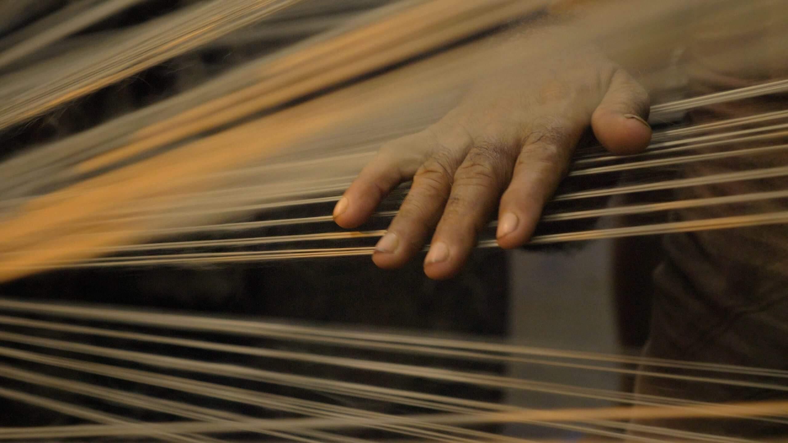 Still from The Golden Thread. A workers hand on jute threads as they pass through the spinning machine
