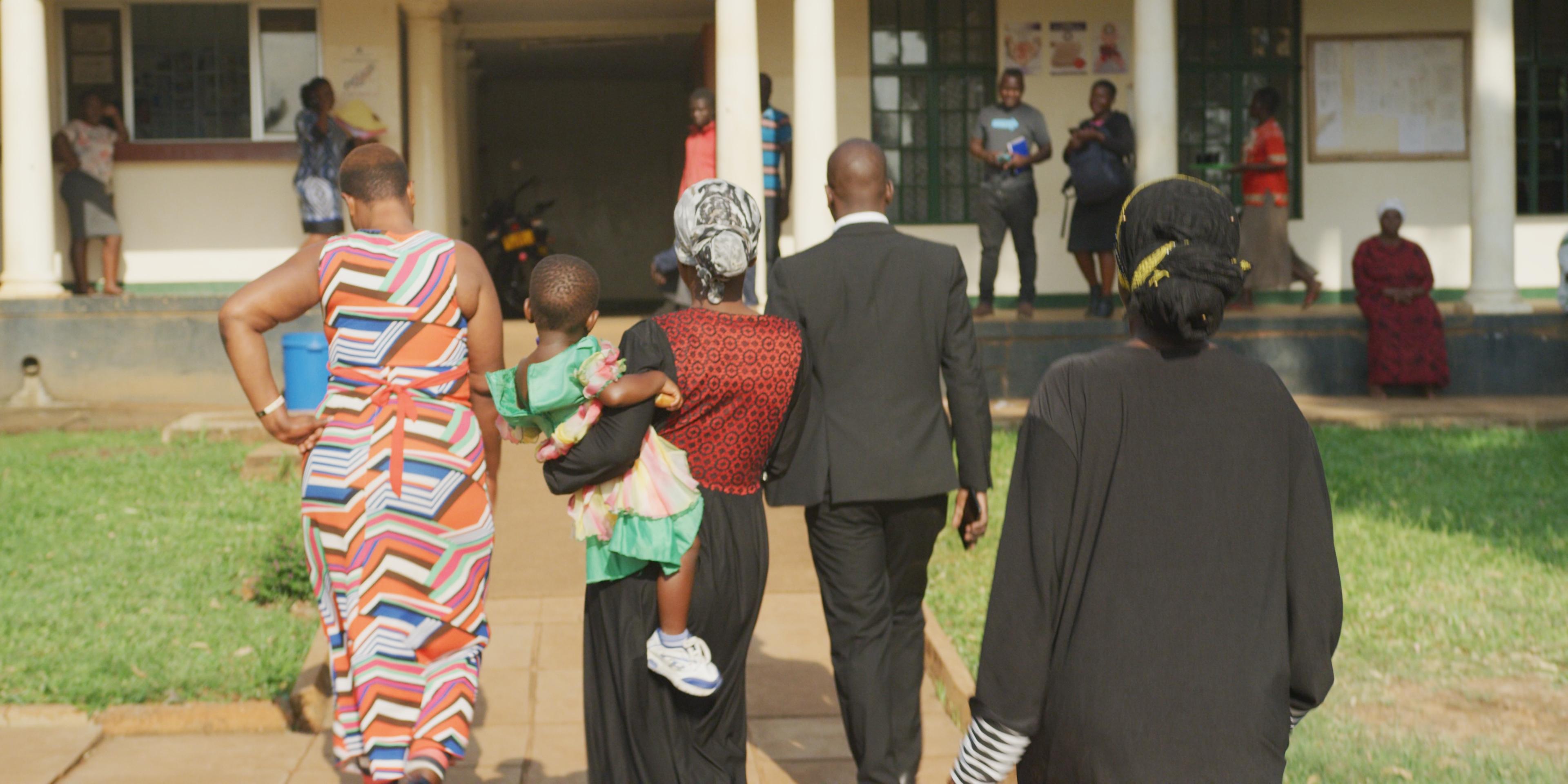 A lawyer enters a courthouse accompanied by three women, one holding a child.