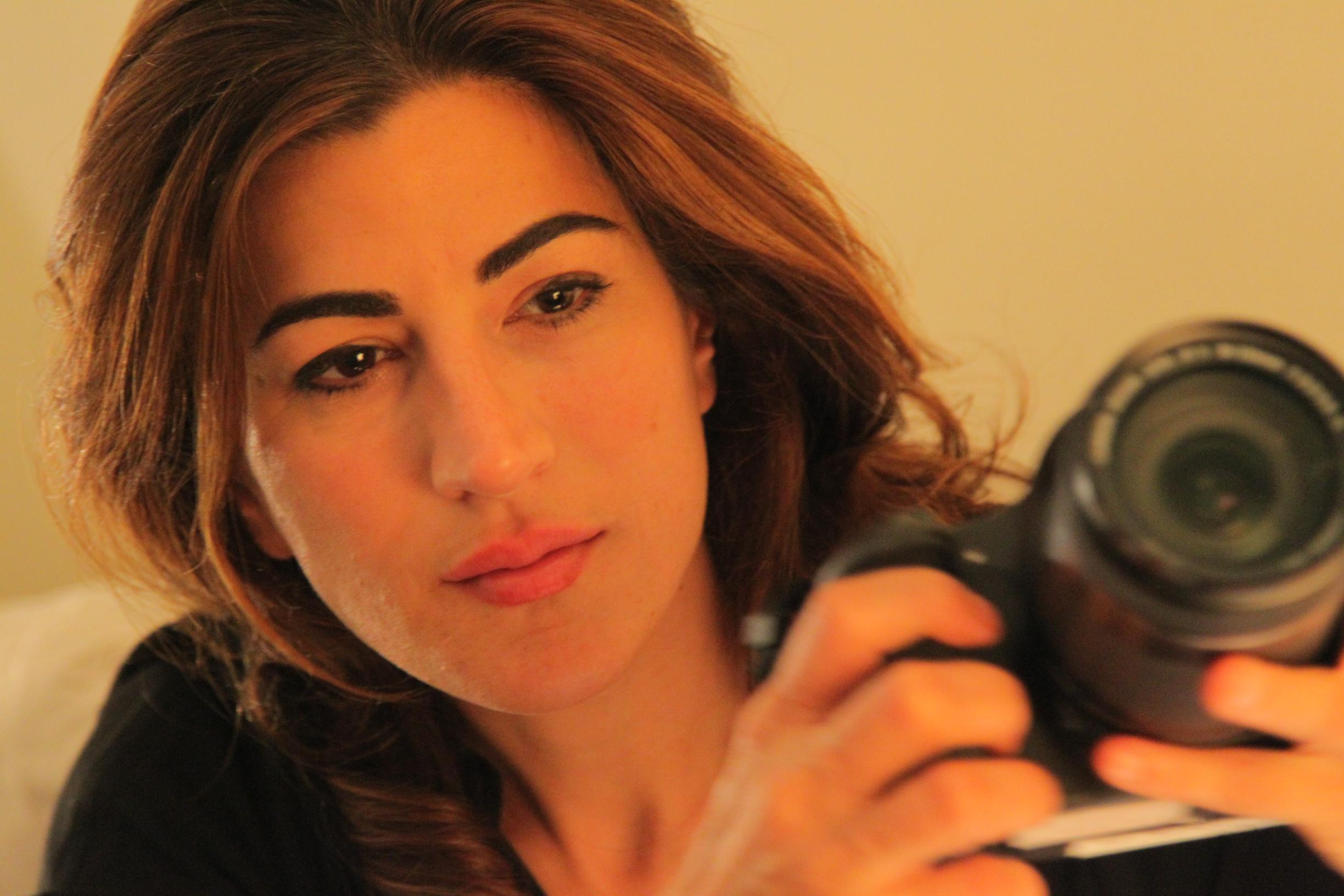 Jehane Noujaim looks past the camera. She is holding a camera whilst looking into the distance.