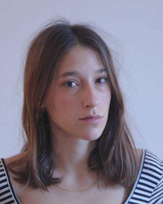 Image of woman with mid-length brown straight hair wearing a blue and white stripped shirt looking at the camera.