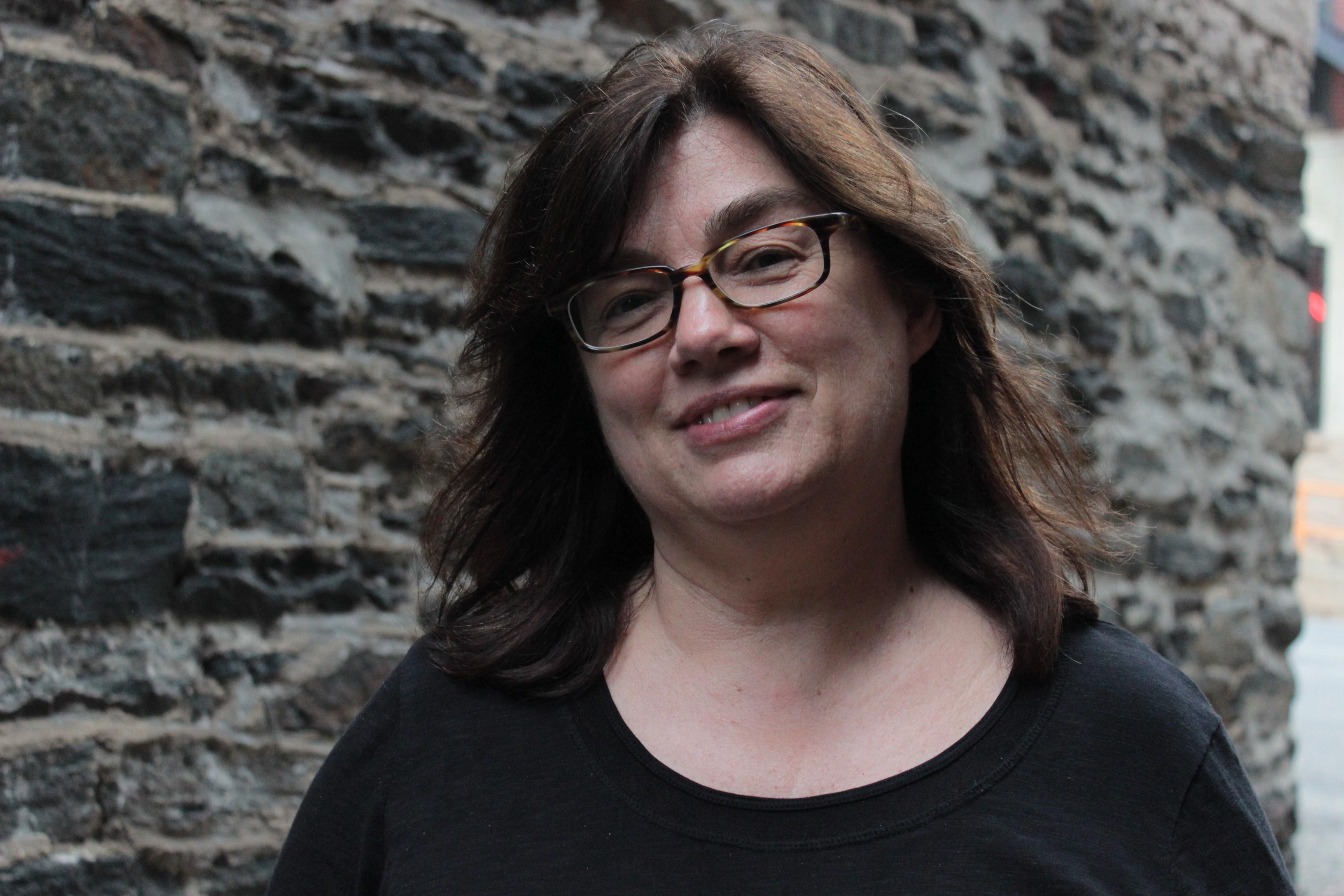 Mary Dore looks at the camera and smiles. She has thin glasses and brown hair.