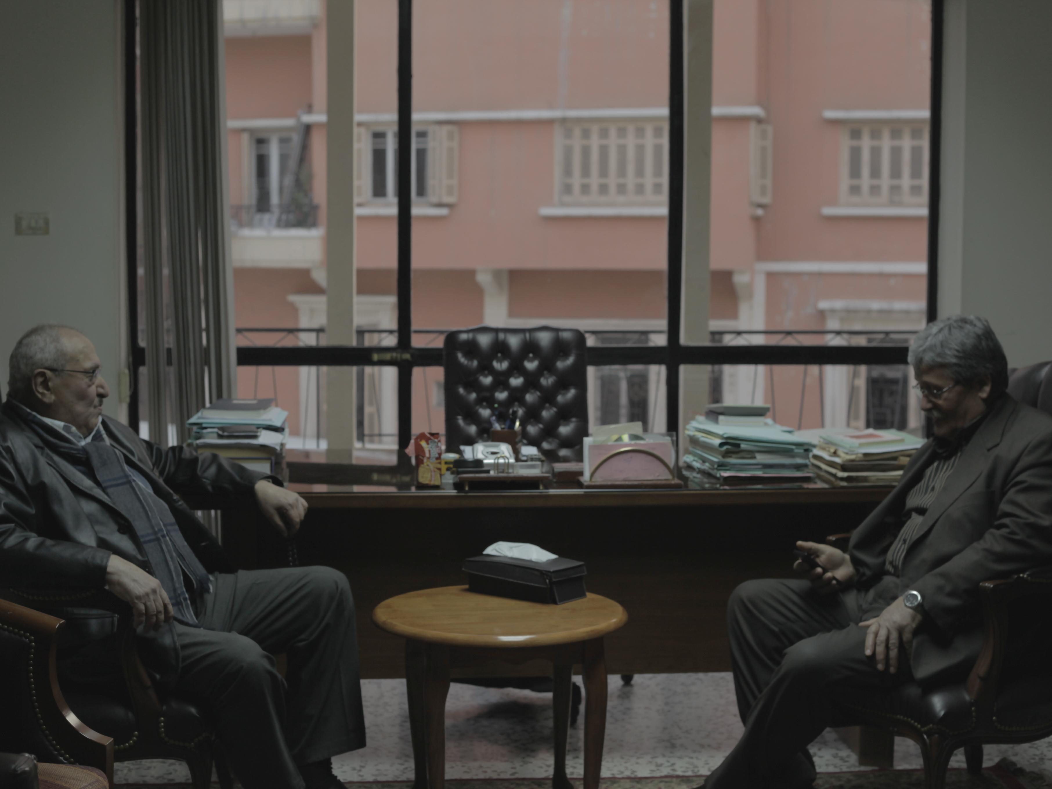 Still from We Are Inside. Two men sit across from each other in an office room.