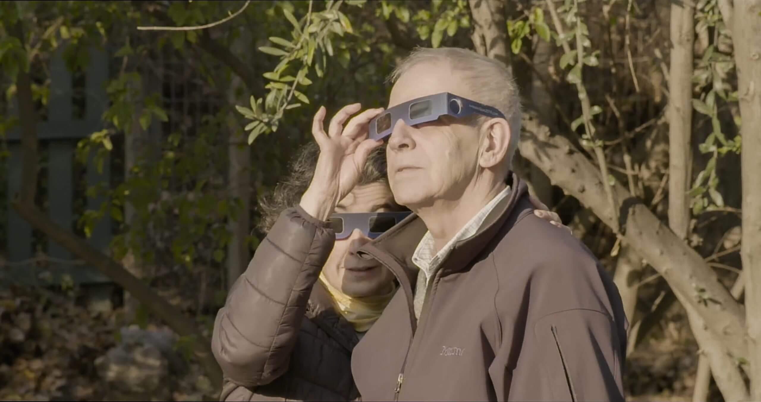 Still from The Eternal Memory. Paulina and Augusto, the main characters of the film, have solar eclipse sun glasses as they watch the event that was happening at that moment.