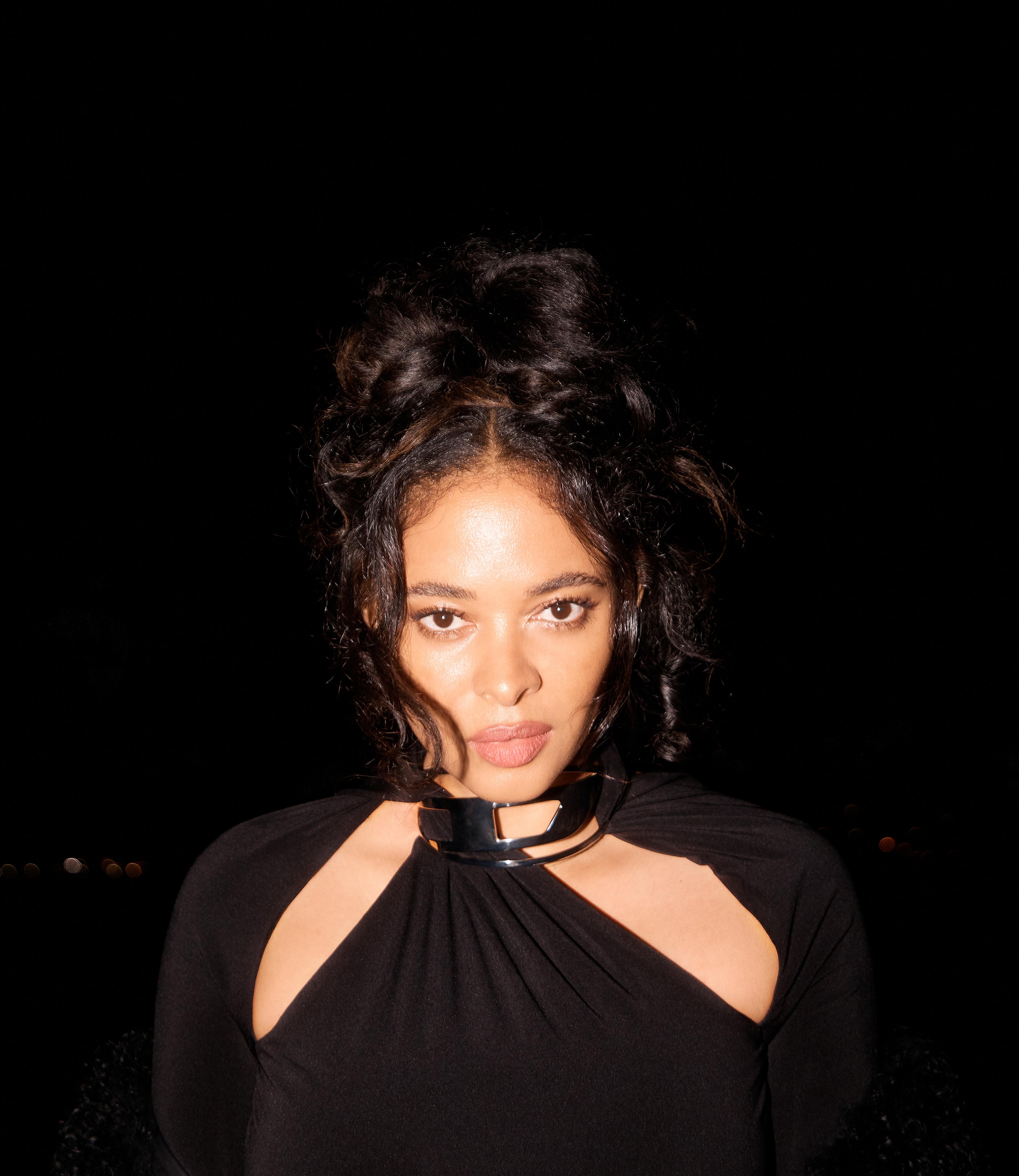 A portrait of a woman in front of a black backdrop looking into the camera.