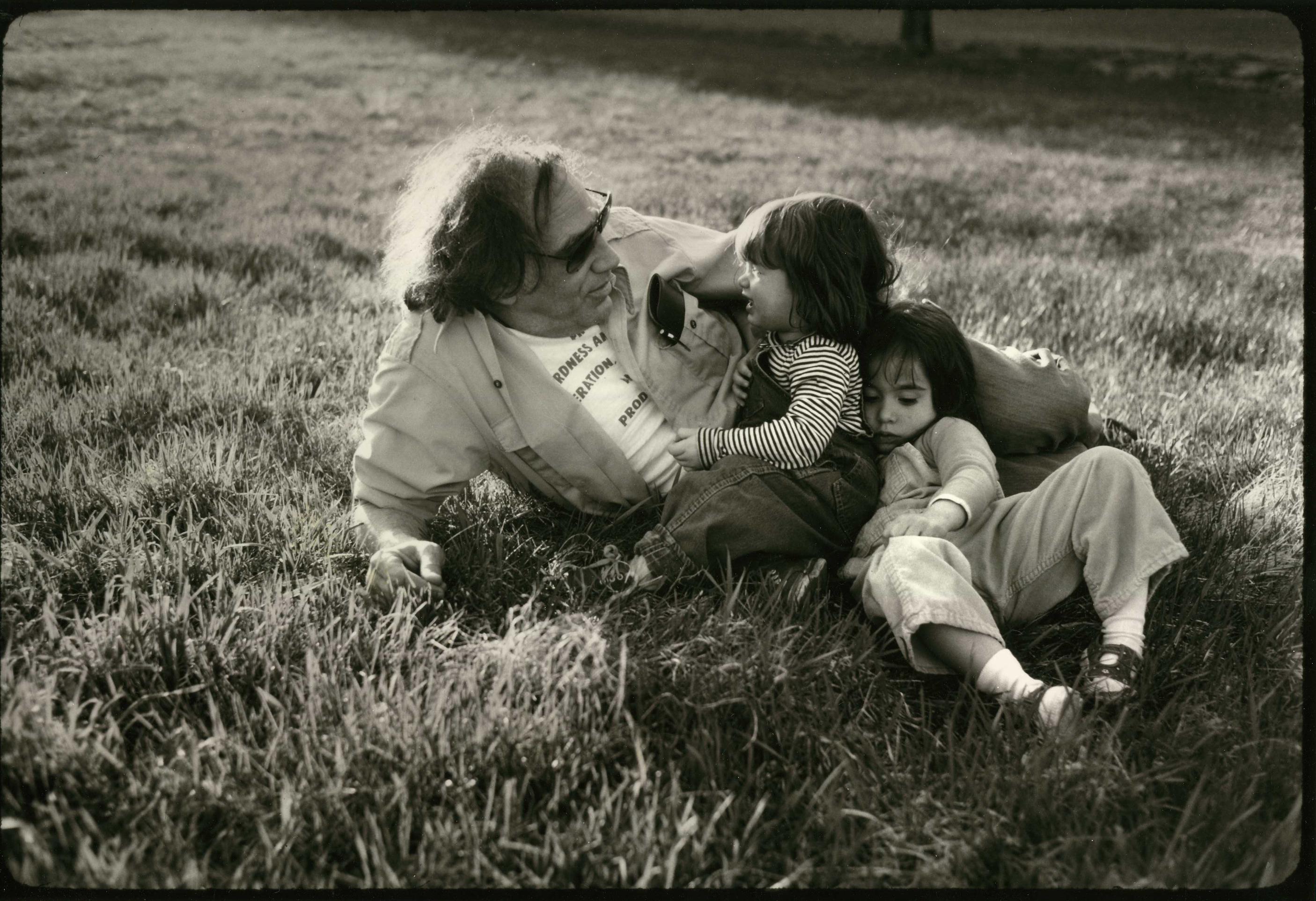 An archival photo of a man sitting on the grass with his two young daughters.