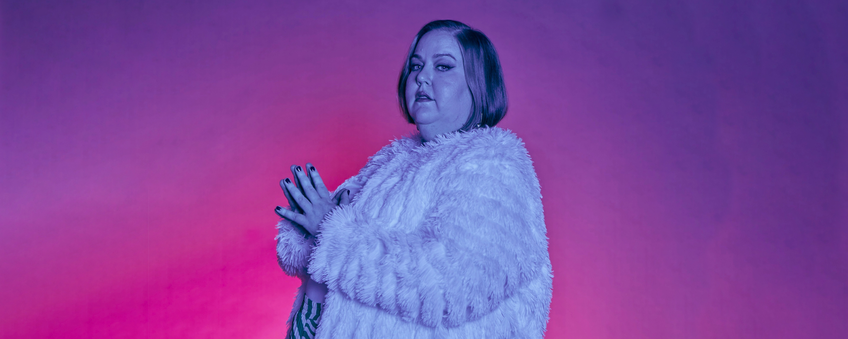 Aubrey Gordon stands in front of a pink and purple gradient backdrop.