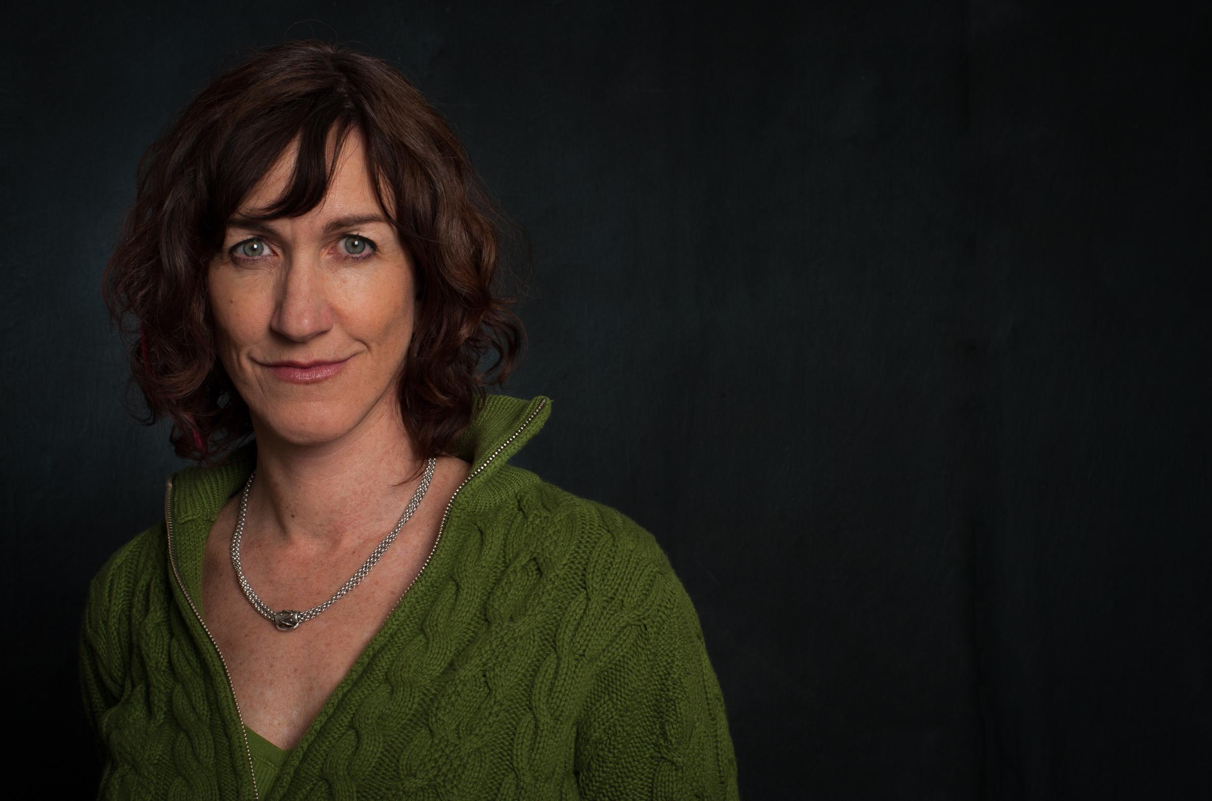 Suzan Beraza has short brown hair. Shes looking at the camera in front of a deep blue background.