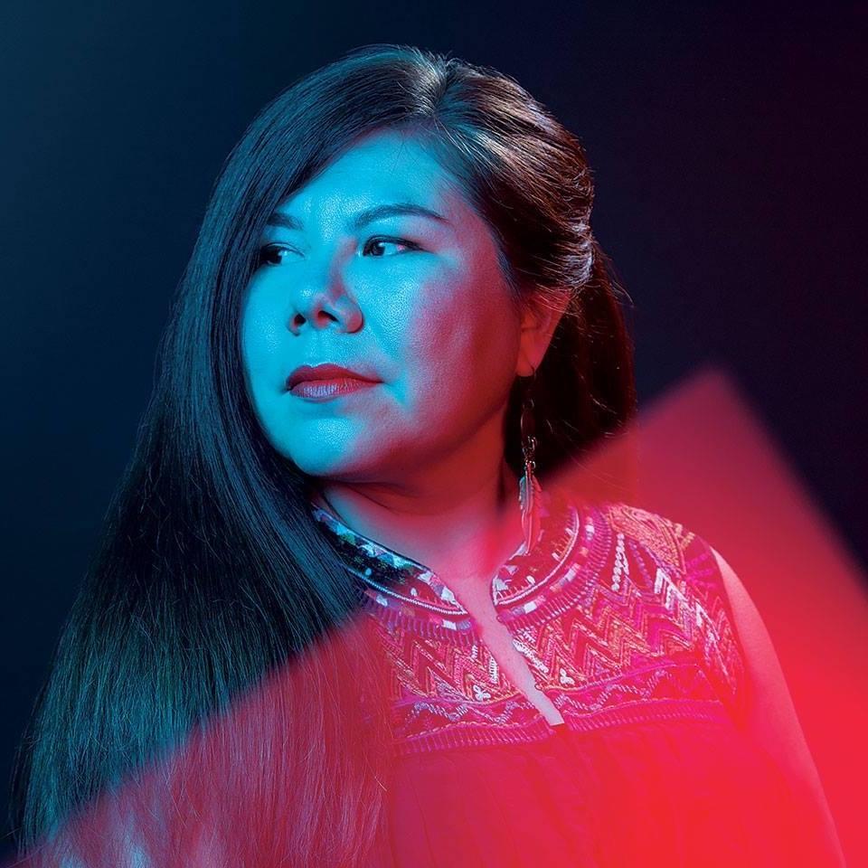 Chelsea Hernandez looking left of the camera in a side profile. She has long dark hair and is wearing red lipstick with an embroidered blouse. Black and white portrait.