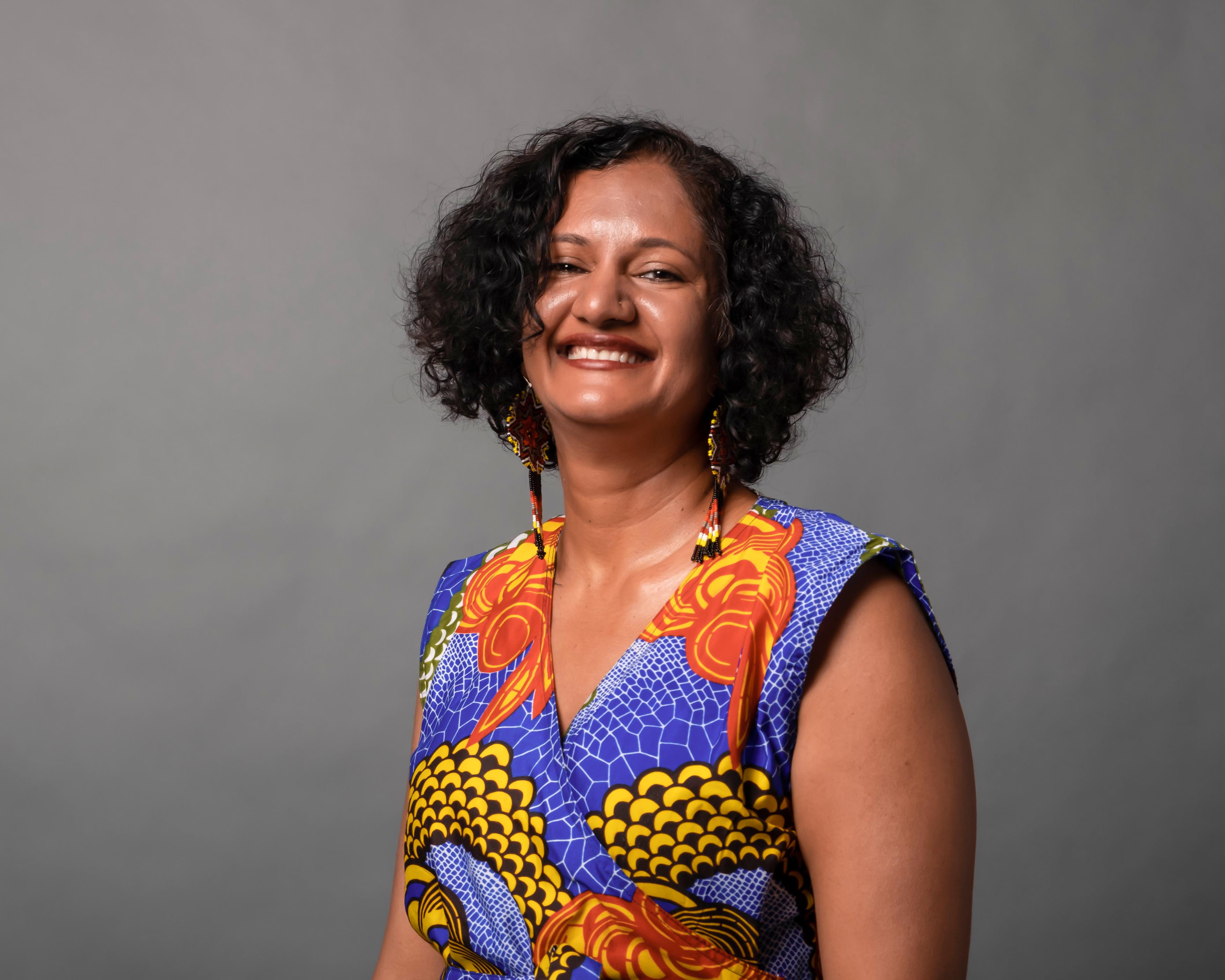 Hemal Trivedi smiles at the camera in front of a grey background.