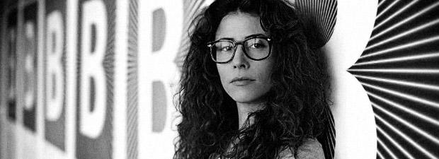 Alma Har'el looks directly at the camera. She is wearing thick glasses and does not smile. The Portrait is in Black and White.